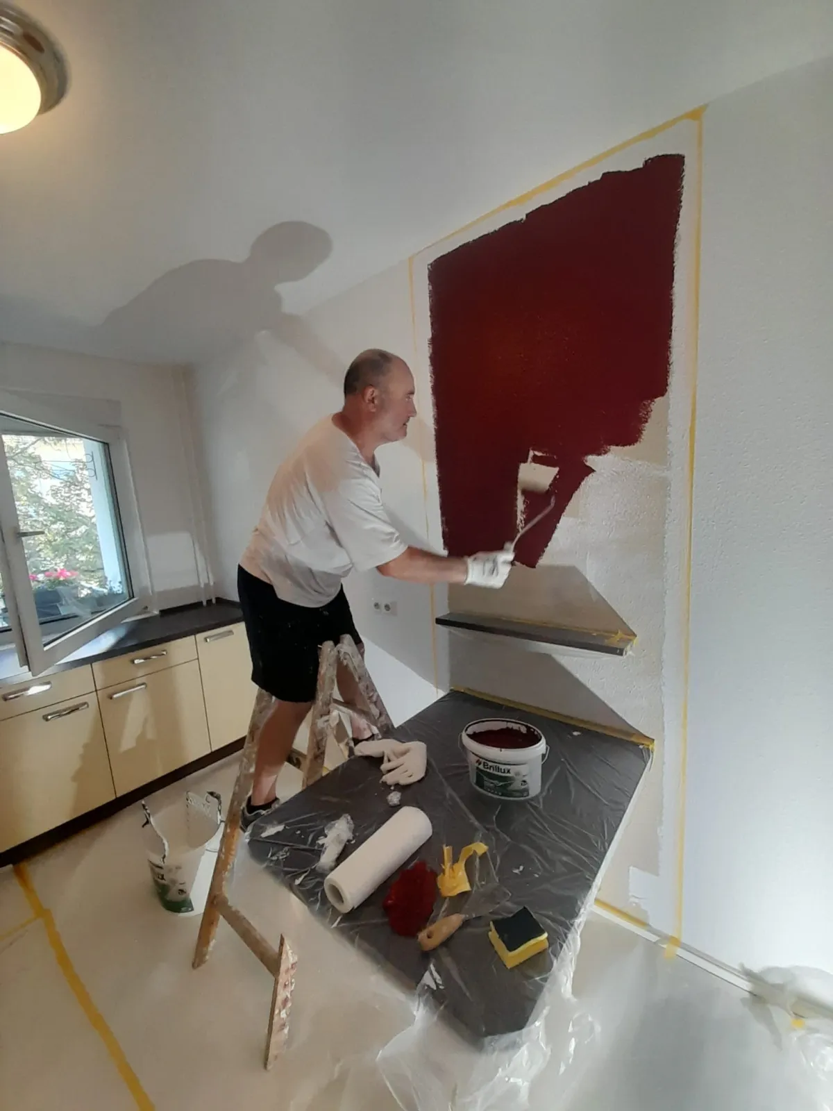 Andymen-Maler auf Leiter streicht Akzentwand Weinrot in K&uuml;che Erlensee mit Brillux-Material