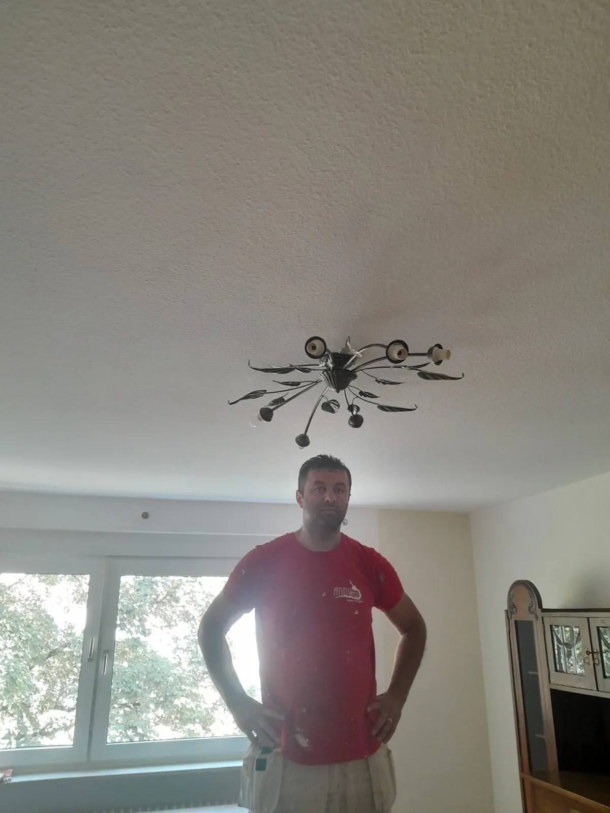 Maler im Andymen-Shirt streicht Wohnzimmer Decke fertig
