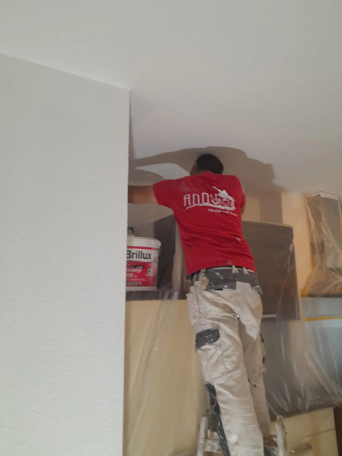 Andymen-Logo auf Ruecken sichtbar Maler streicht Decke mit Brillux-Eimer