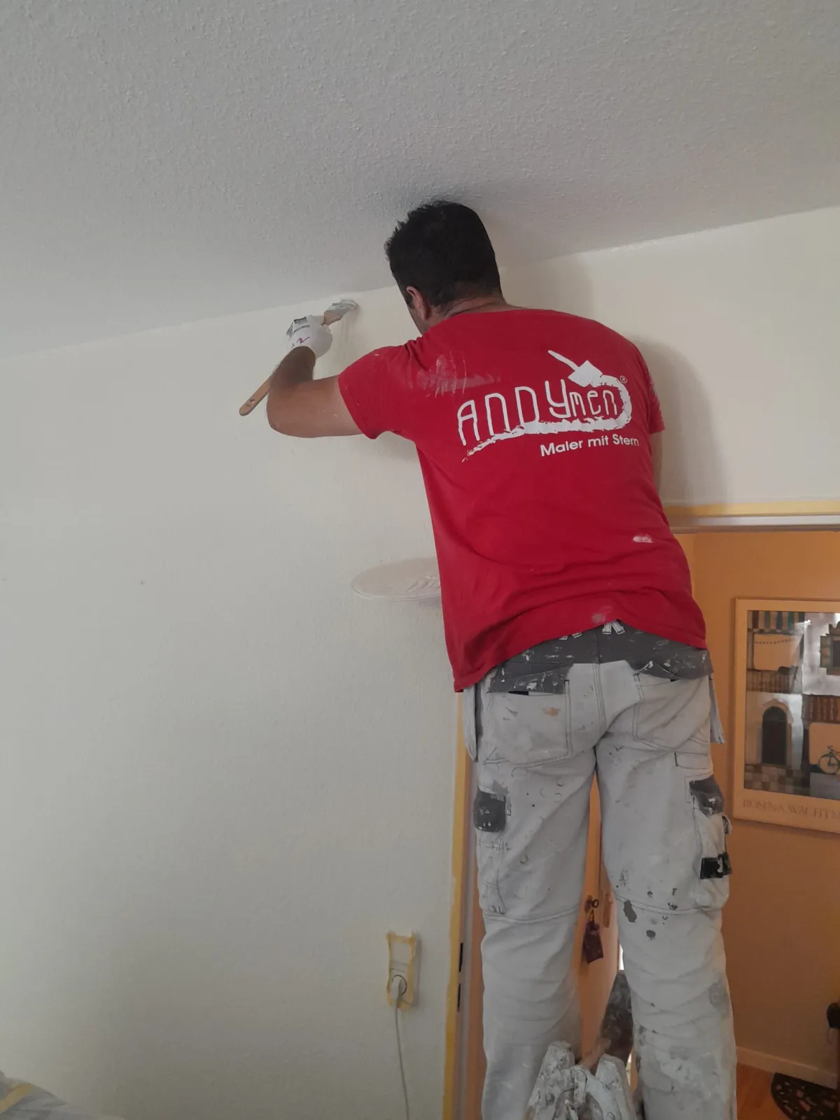 Andymen-Logo perfekt lesbar auf Shirt Maler streicht Wand im Wohnzimmer