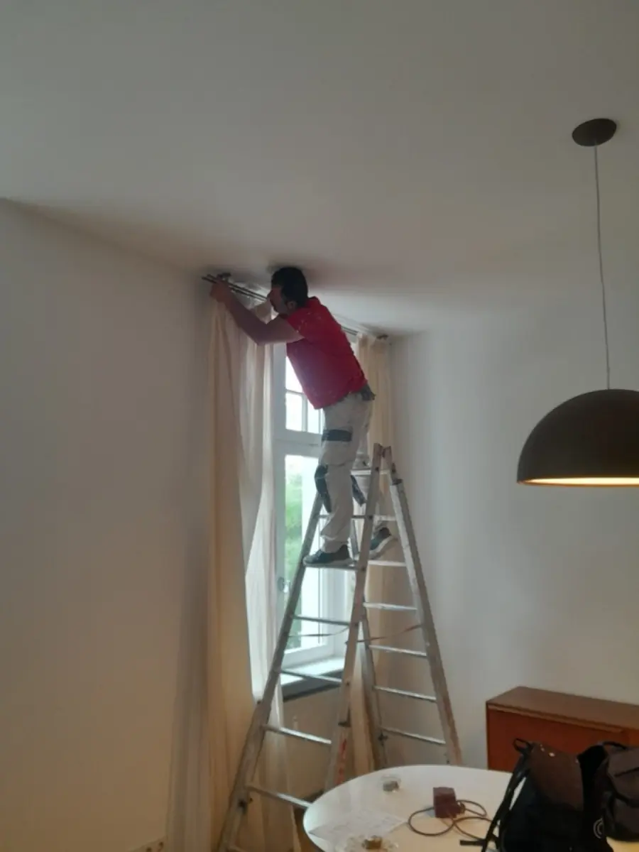 Andymen-Maler auf Leiter bei Gardinenarbeiten &mdash; Altbau Frankfurt-Nordend, rote Jacke