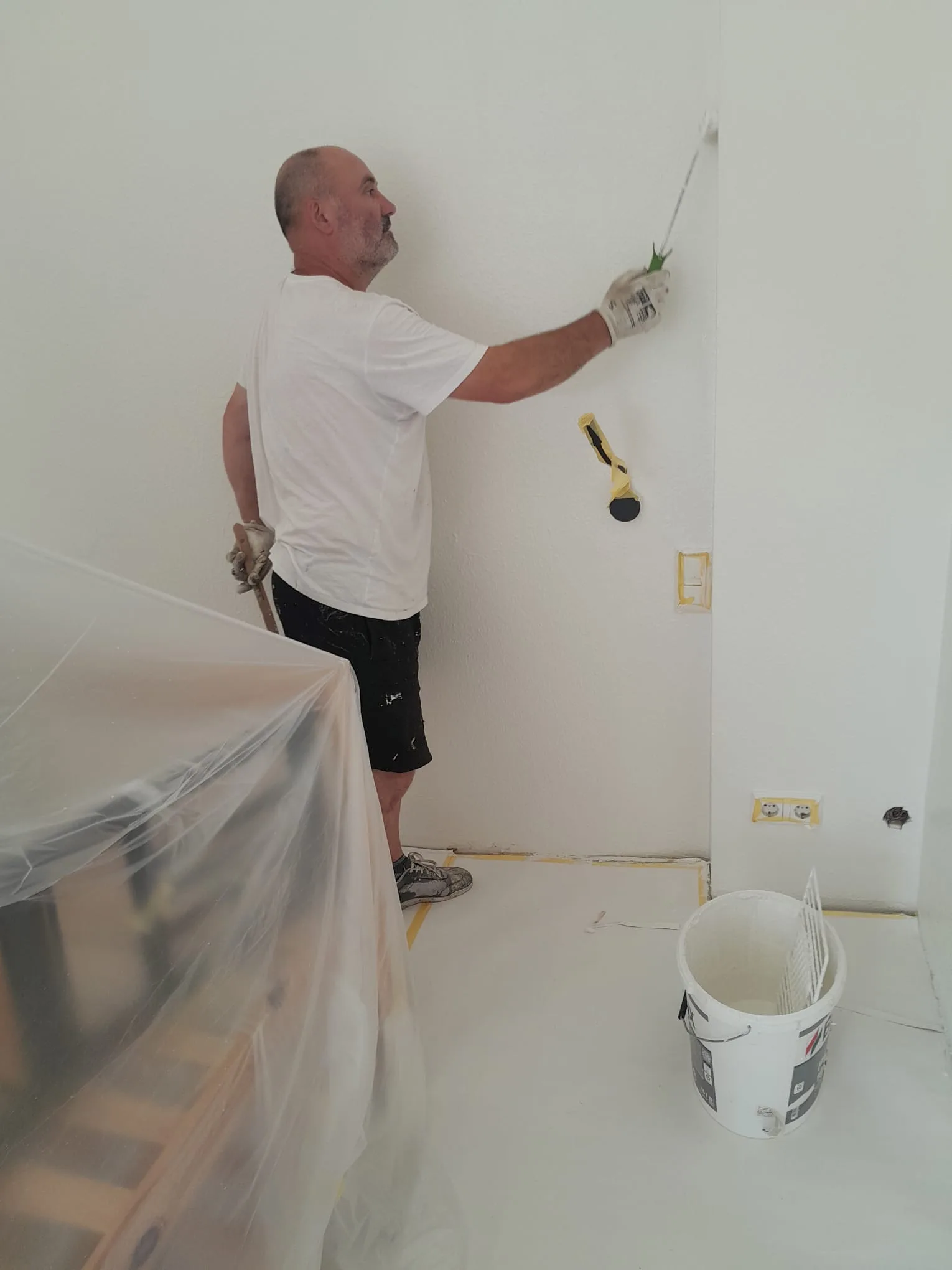 Maler streicht Wand an Steckdosen und Lichtschalter sauber ausgespart Dachgeschosswohnung