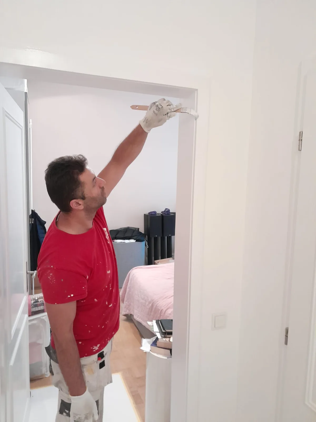Andymen-Mitarbeiter in rotem T-Shirt lackiert T&uuml;rzarge mit Rolle &mdash; Altbau Frankfurt-Nordend