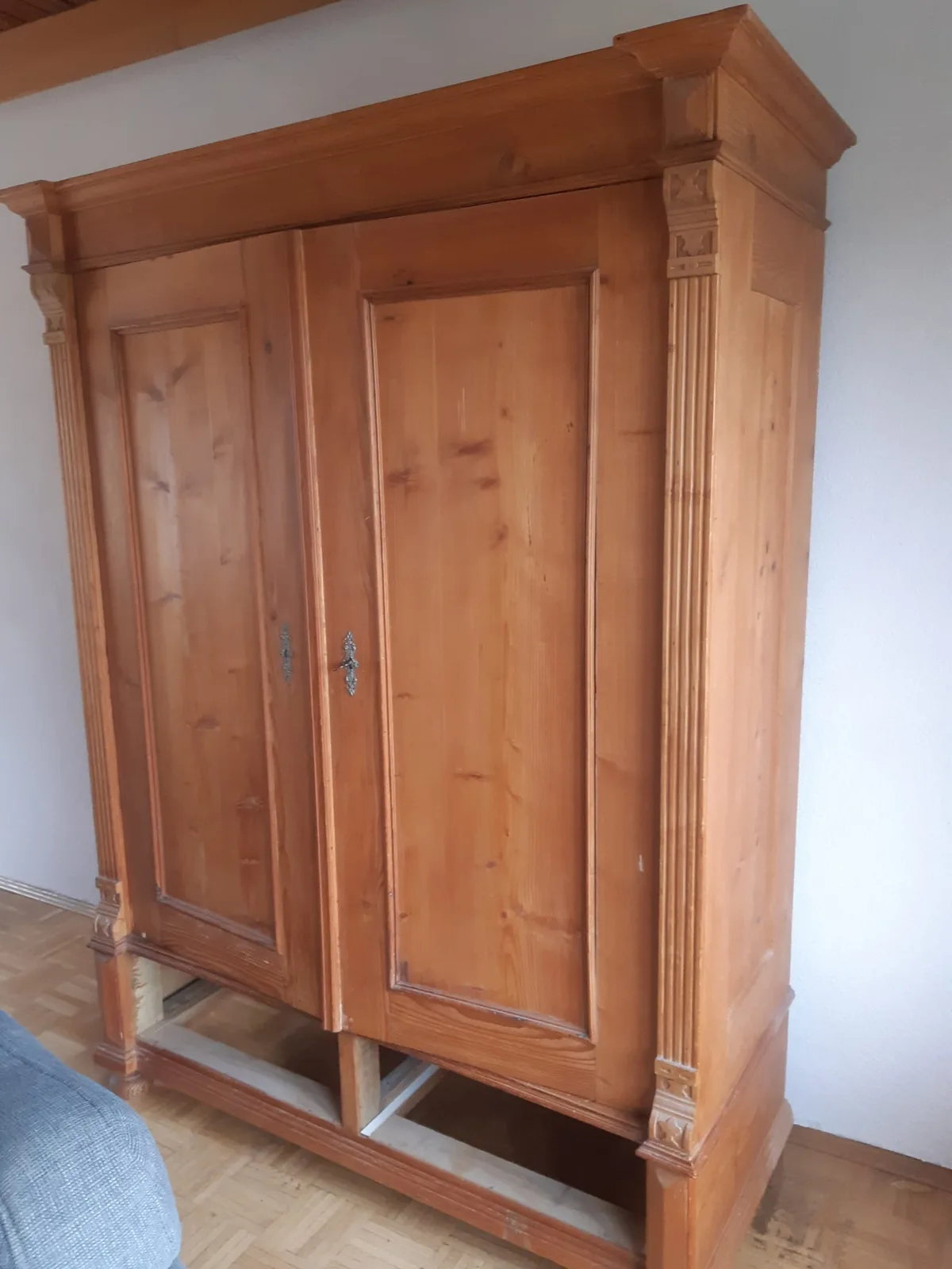 Wohnzimmer vor Renovierung – blaues Ecksofa und antiker Kiefernschrank